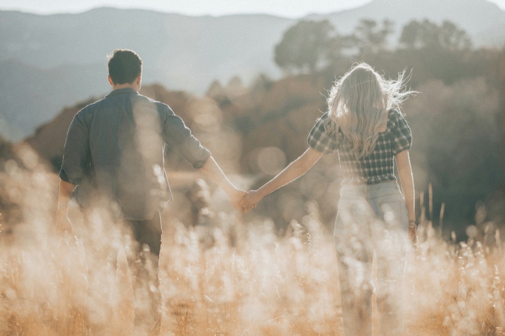 A couple walking hand-in-hand through tall golden grass.